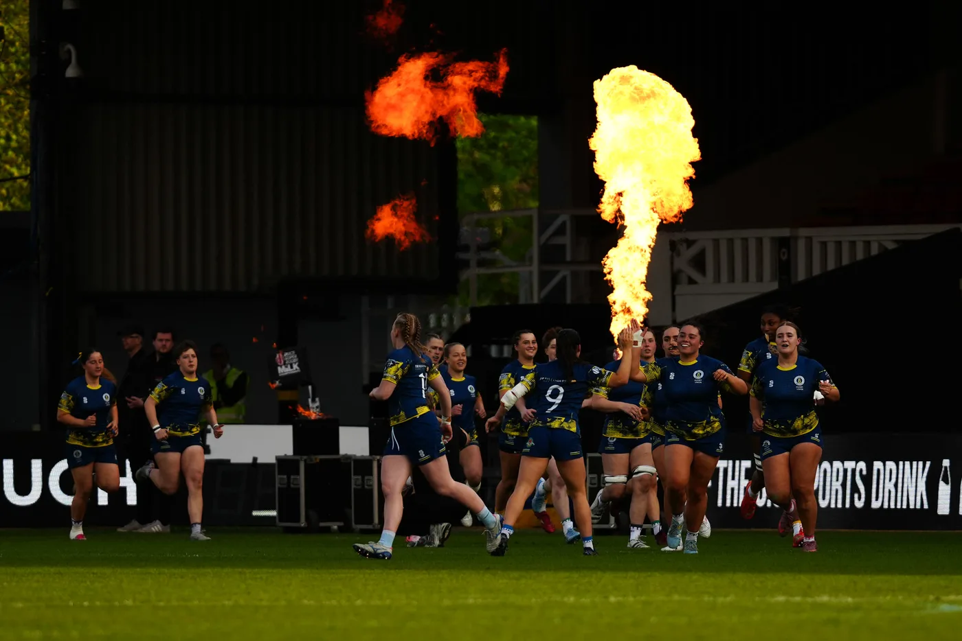 Players running out on to the pitch as flames shoot up behind them before the 2026 Women's BUCS Super Rugby final