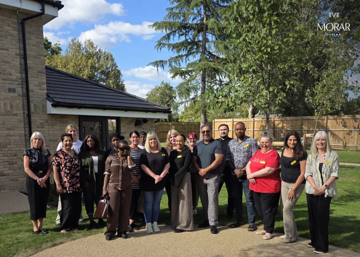 A large group of Fernacre Court staff standing together on a path in the home's garden on a sunny day