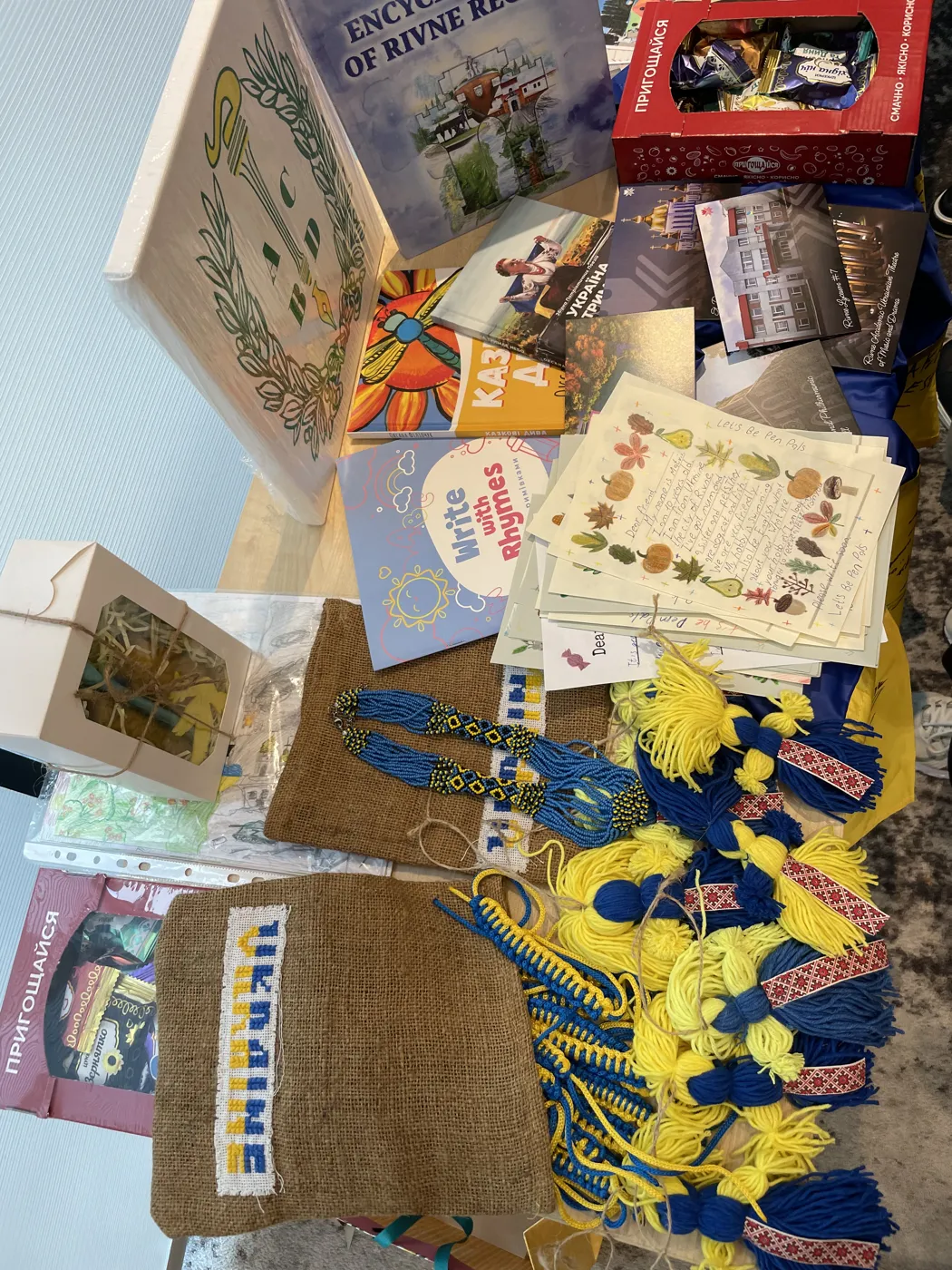 Blue and yellow woven bracelets, a hessian bag, handmade cards and books spread on a table