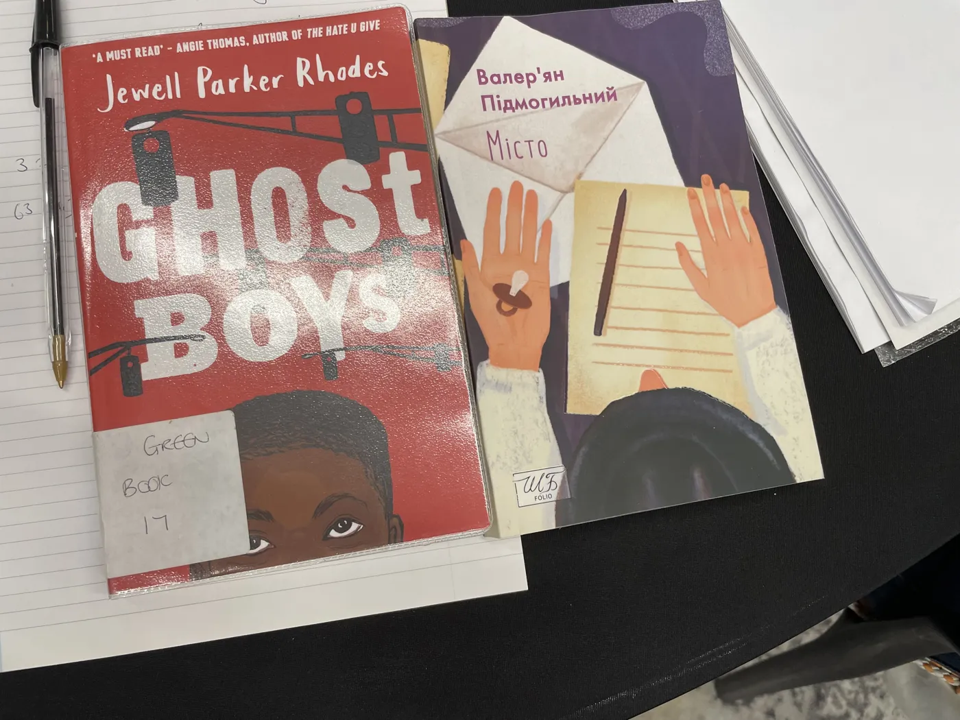 A copy of Ghost Boys by Jewell Parker Rhodes lying next to a Ukrainian novel, Misto by Valerian Pidmohylny, on a table